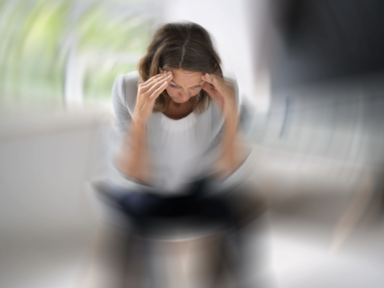 Eine Frau fasst sich an die Stirn, alles dreht sich um sie herum.