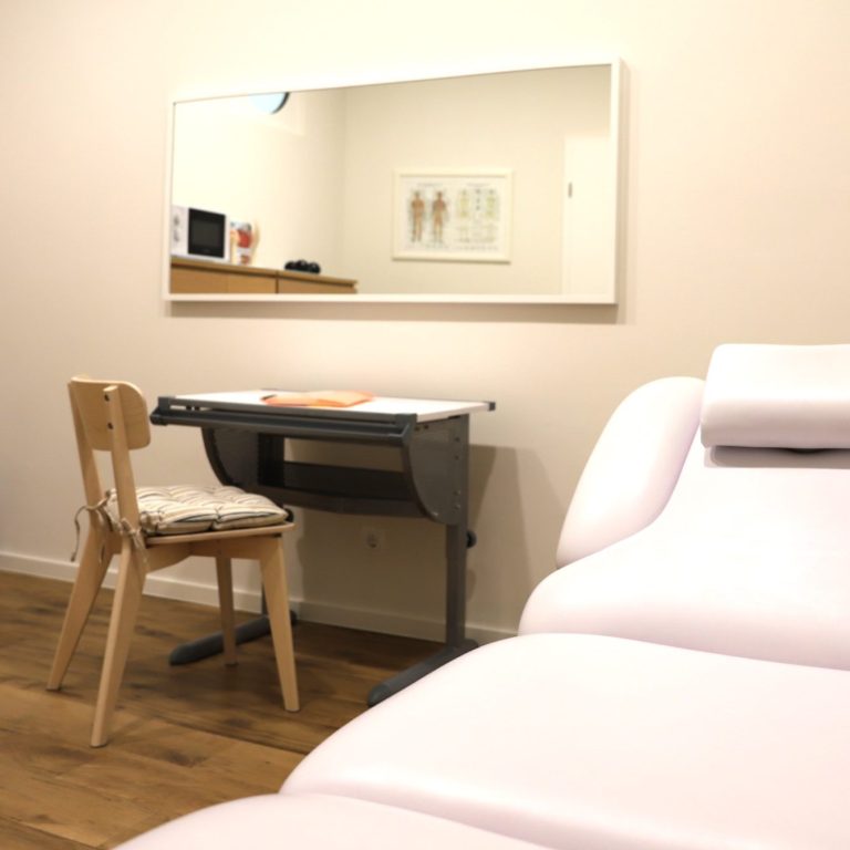 Ergotherapeutische Praxis Robert Steiger Eine Massageliege, ein Stuhl vor einem kleinen Tisch und einem Spiegel.