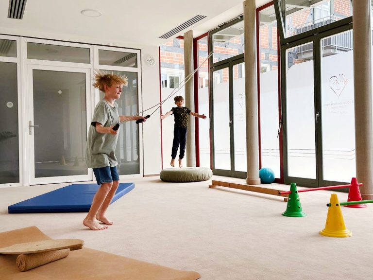 Ergotherapeutische Praxis Robert Steiger Zwei Jungen turnen in einem hellen Sportraum mit hohen Fenstern.