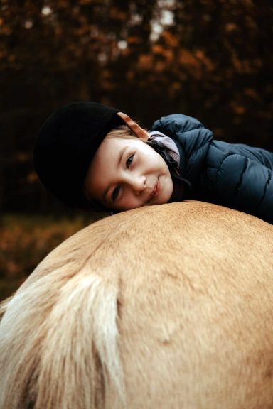 Reittherapie Ivenack Ein kleines Mädchen hängt über der Kuppe eines Pferdes und ist glücklich.