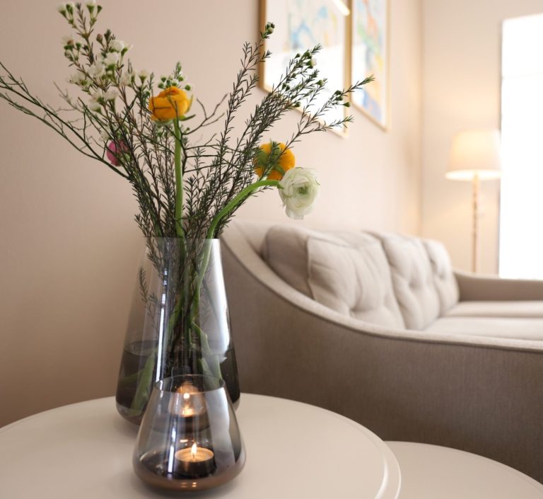 Praxisräume Ergotherapie Eine Glasvase mit Schnittblumen steht auf einem kleinen Tisch vor einer Couch, warme, helle Farben