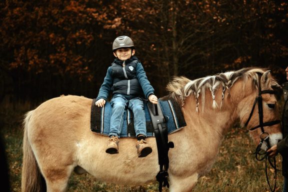 Reittherapie Ivenack Ein Junge sitzt seitlich auf einem Pferd und schaut stolz.
